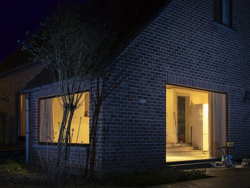 Maison en brique la nuit, deux fenêtres éclairées de l’intérieur.