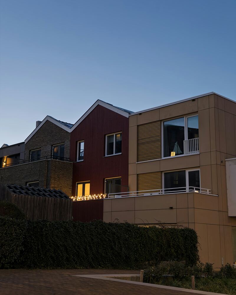 Maisons neuves en brique et bardage au crépuscule, quelques fenêtres éclairées.