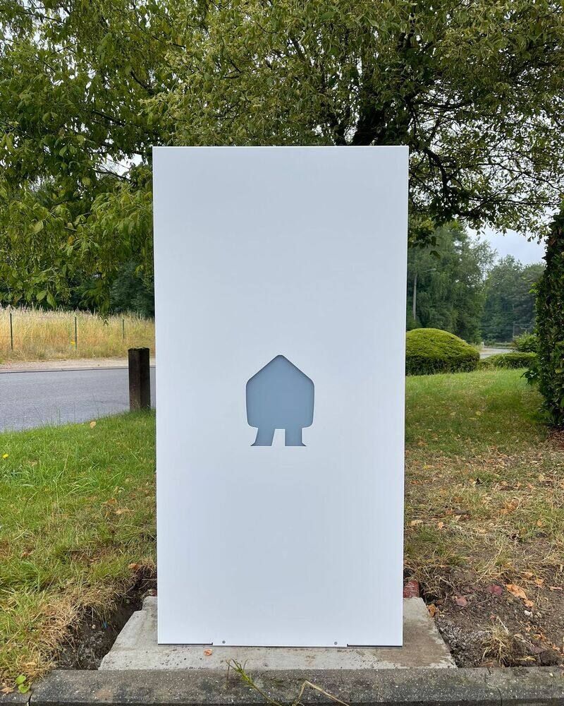 Borne de recharge sur pied, blanche, installée sur une pelouse devant des arbres.